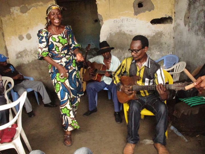 Members of the band Bakolo Music International rehearsing with guitars while a singer dances, Kinshasa