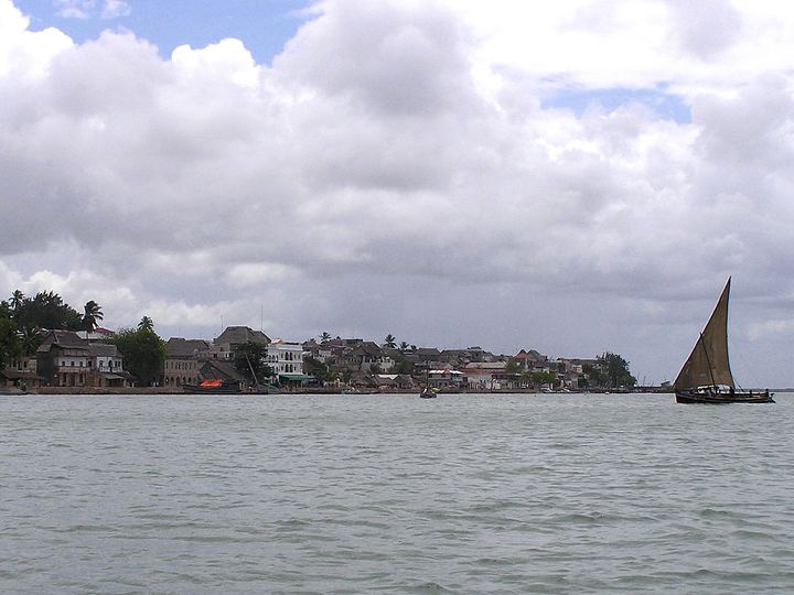 The seafront of Lamu Town in Kenya seen from the water, with a dhow under sail