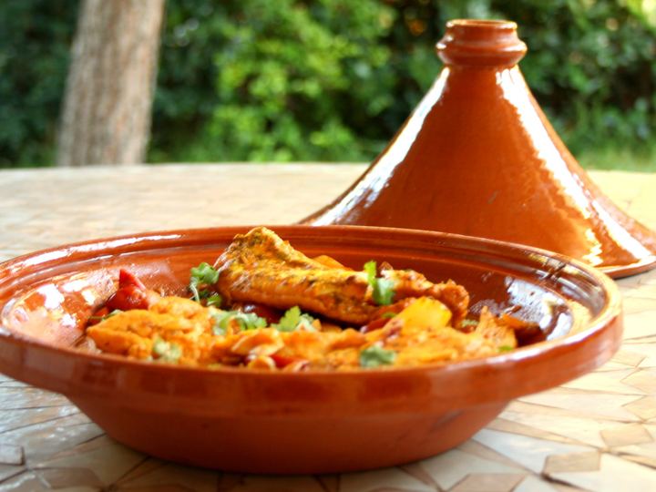 A Moroccan chicken tagine served in a terracotta dish beside its tall conical lid