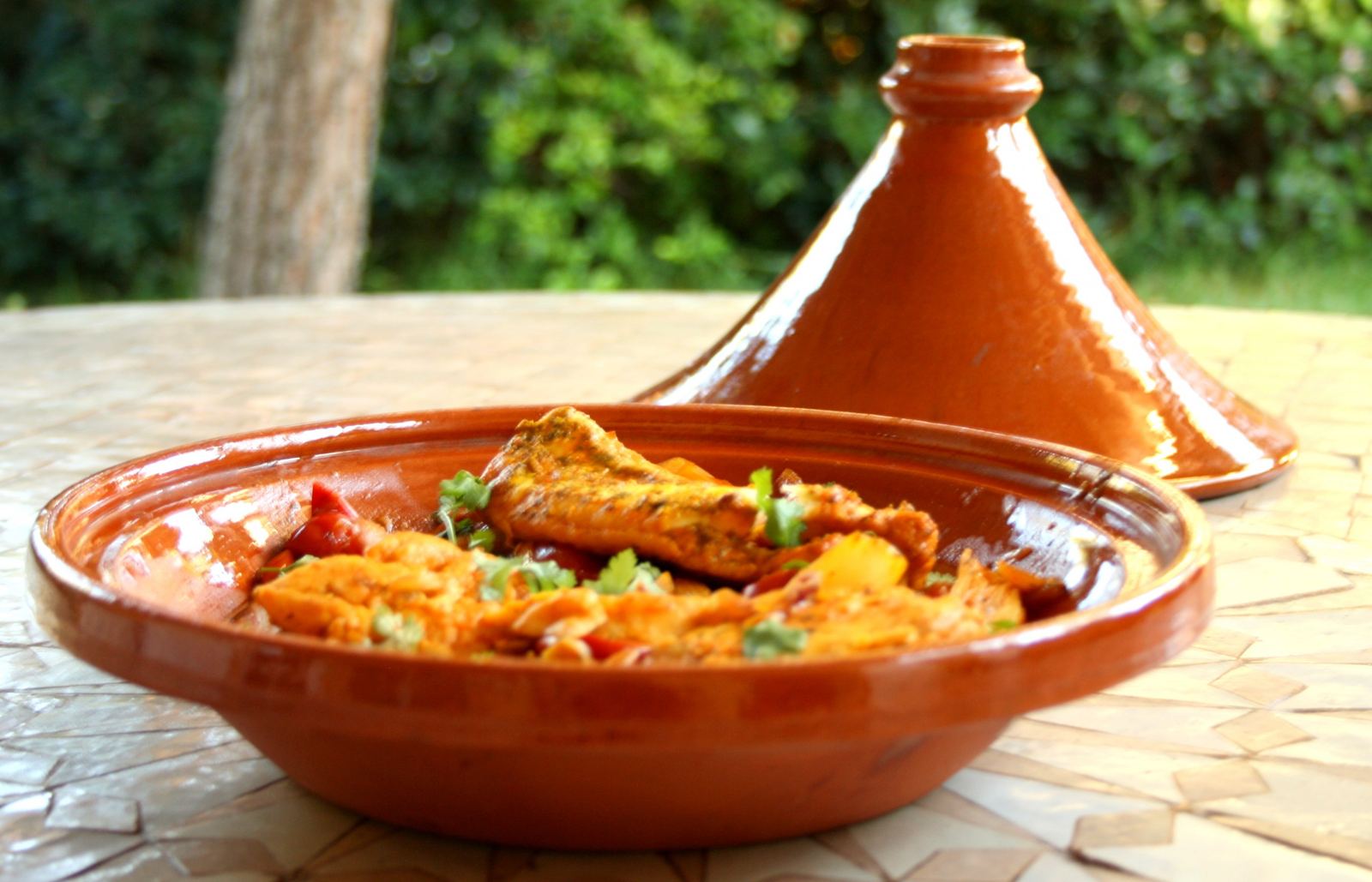 A Moroccan chicken tagine served in a terracotta dish beside its tall conical lid